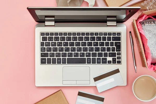 Online shopping concept on pink desk table with laptop, credit cards, parcels and clothes. Top view.