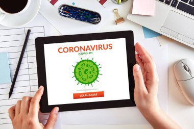Eller koronavirüslü dijital tablet bilgisayar kullanıyor. İş masasının üzerinde Coperid-19 konsepti var. Üst görünüm