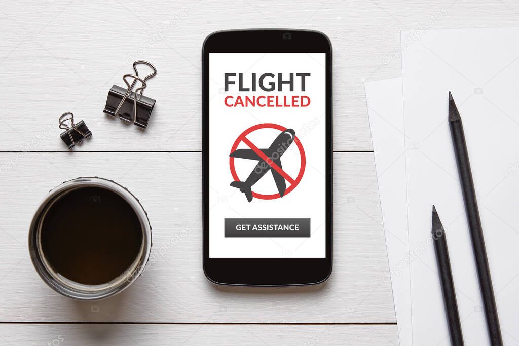 Flight cancelled concept on smart phone screen with office objects on white wooden table. Top view