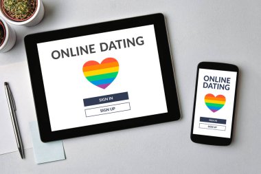 Tablet üzerindeki LGBT randevu uygulaması konsepti ve gri masanın üzerindeki cep telefonu ekranı. Eşcinsel online randevu. Üst görünüm
