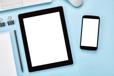Dikey tablet bilgisayarın ve mavi yüzeyi boş beyaz ekranlı akıllı telefonun görüntüsü. Düz yatıyordu