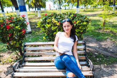 Parkta elinde defterle oturan genç bir kadın.