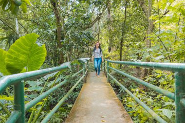 Kadın ormanda küçük bir köprü üzerinde yürüyor.
