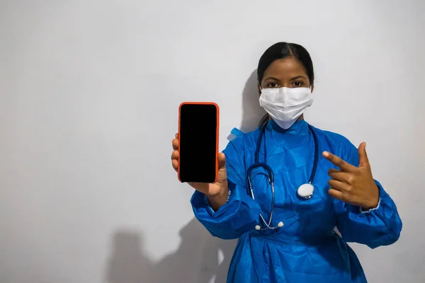 医学界的年轻黑人妇女 身穿蓝色长袍 戴着显示手机屏幕和指点的面具 — 图库照片