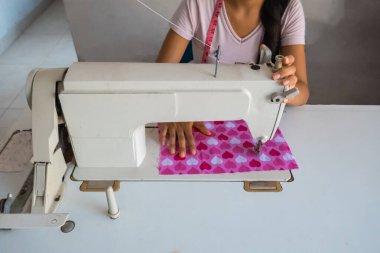 Atölyede dikiş makinesiyle dikiş diken genç bir kadın.