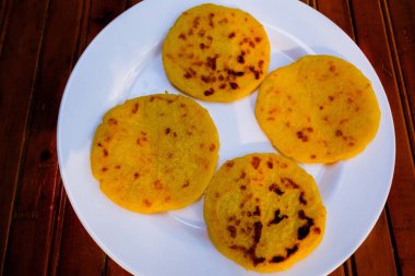 Koyu ağaçta doğal ışıkla çekilmiş arepa plakası. Arepalar sarı mısır unundan yapılmıştır. Kolombiya yemeği.