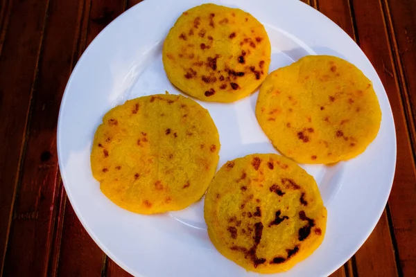 Koyu ağaçta doğal ışıkla çekilmiş arepa plakası. Arepalar sarı mısır unundan yapılmıştır. Kolombiya yemeği.