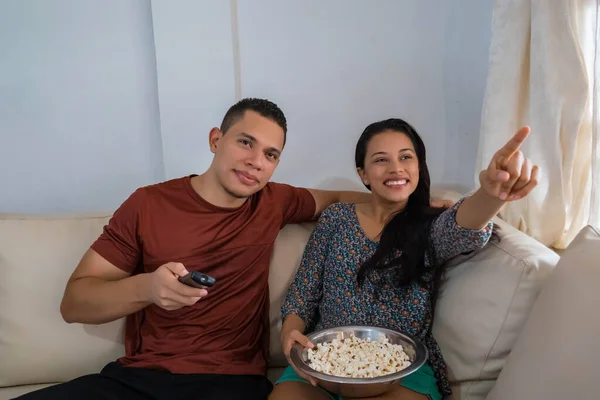 A picture of a young Latino couple watching TV at home