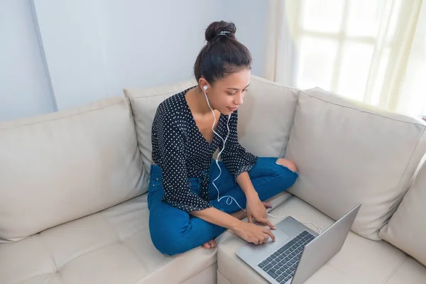 professional entrepreneur working at home through a laptop, a young woman using a laptop device while sitting on the couch, concept of work process