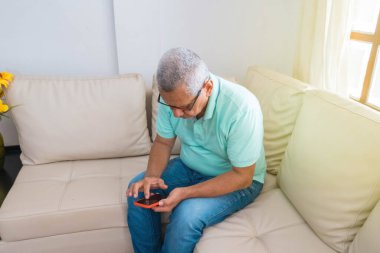 Evde cep telefonuyla mesaj atan yaşlı bir adam.