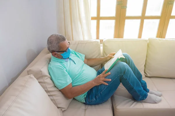 old man in a medical mask reading a book at home