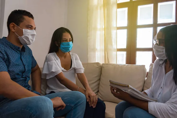 Financial consultant presenting a business investment to a young, smiling couple wearing a medical mask