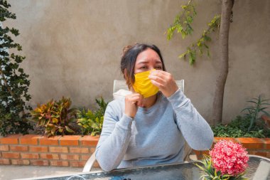 Olgun bir kadın bahçede oturmuş, maskesini düzeltiyor.