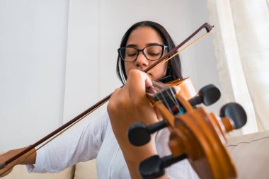 Güzel ve tatlı Latin kadın evde keman çalıyor.