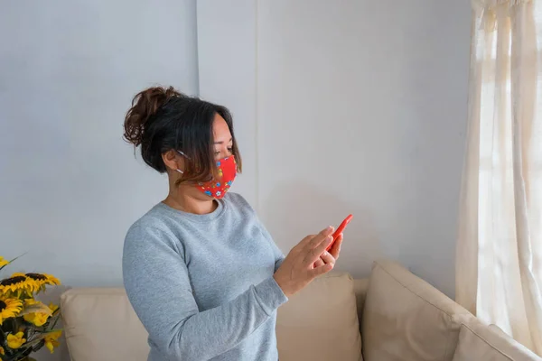 Latino Kvinna Stående Med Ansiktsmask Vardagsrummet Stirrar Sin Mobiltelefon — Stockfoto