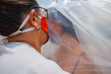 Anne ve kızı plastik bir çarşaf arasında sarılıyorlar. Sosyal uzaklık kavramı