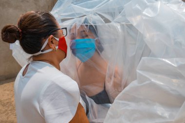 Anne ve kızı çamaşır ipine asılı plastik bir çarşafla ayrılmış. Sosyal uzaklık kavramı
