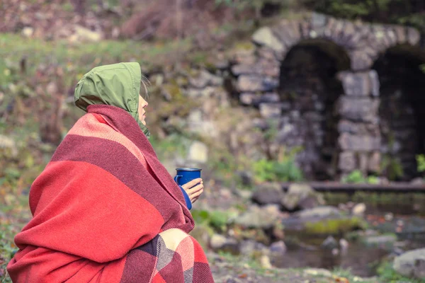 Путешественник пьет горячий чай или кофе в лесу осенью обертывание в клетчатое шерстяное одеяло — стоковое фото
