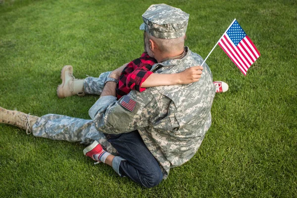 Soldado americano reunido com o filho sentado na grama verde e abraçando uns aos outros — Fotografia de Stock