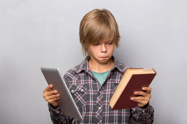 Мальчик держит книгу и планшет изолированы на сером фоне — стоковое фото