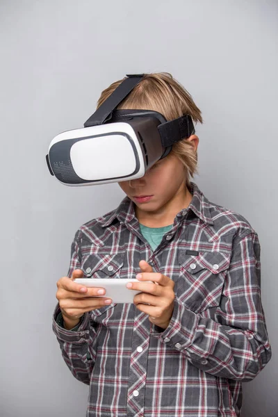 Мальчик в очках виртуальной реальности держит мобильный телефон — стоковое фото