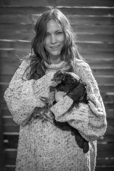 Beautiful woman with flying hair in country holding a hen, focus on face, black and white