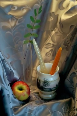 Çaydanlıklar ve sürahiler üzerine dekoratif set, farklı renklerde vazolar ve bir elmayla desenler. Aydınlatılmış perdenin arkasındaki yapraklar ve mumlar