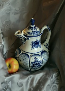Çaydanlıklar ve sürahiler üzerine dekoratif set, farklı renklerde vazolar ve bir elmayla desenler. Aydınlatılmış perdenin arkasındaki yapraklar ve mumlar