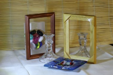 Farklı renklerde cam ve kristal tabaklar, yeşil, mavi, şeffaf şarap bardakları ve masa üzerinde peçeteler ve çerçevelerle renkli cam toplarla şamdanlar.