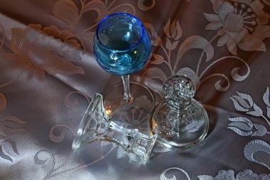 Farklı renklerde cam ve kristal tabaklar, yeşil, mavi, şeffaf şarap bardakları ve masa üzerinde peçeteler ve çerçevelerle renkli cam toplarla şamdanlar.