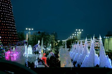 Şehrin şehir gece manzarası, binaların aydınlatılmış mimarisi ve merkezde buz figürleri ve cazibeleriyle yeni yıl kutlamaları.