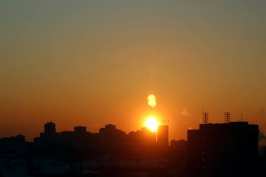 Şehir üzerinde gün doğumu ufukta kırmızı, turuncu ve sarı renkli koyu renkli binalar var.