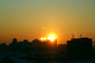 Şehir üzerinde gün doğumu ufukta kırmızı, turuncu ve sarı renkli koyu renkli binalar var.