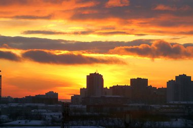 Kış sabahı, yükselen güneş ve sarı, turuncu ve kırmızı bulutlarla şehirde gelişmenin arka planında