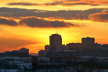 Kış sabahı, yükselen güneş ve sarı, turuncu ve kırmızı bulutlarla şehirde gelişmenin arka planında