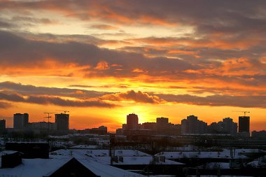 Kış sabahı, yükselen güneş ve sarı, turuncu ve kırmızı bulutlarla şehirde gelişmenin arka planında