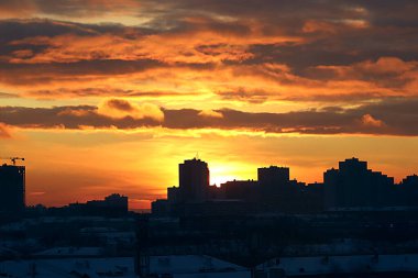 Kış sabahı, yükselen güneş ve sarı, turuncu ve kırmızı bulutlarla şehirde gelişmenin arka planında