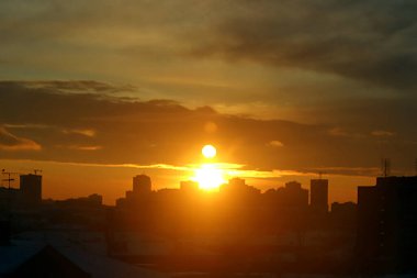 Kış sabahı, yükselen güneş ve sarı, turuncu ve kırmızı bulutlarla şehirde gelişmenin arka planında