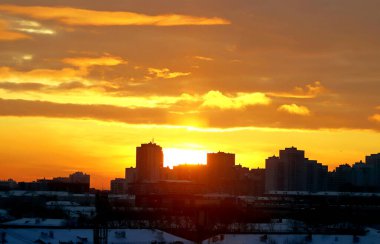 Kış sabahı, yükselen güneş ve sarı, turuncu ve kırmızı bulutlarla şehirde gelişmenin arka planında