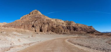 Boş çöl yolunda dağlar ve mavi gökyüzü arka planda.