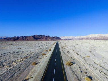 Çöl yolu, kuru çöl manzarasıyla çevrili iki şeritli bir yolun havadan görüntüsü.