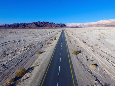 Çöl yolu, kuru çöl manzarasıyla çevrili iki şeritli bir yolun havadan görüntüsü.