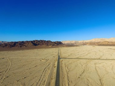 Çöl yolu, kuru çöl manzarasıyla çevrili iki şeritli bir yolun havadan görüntüsü.