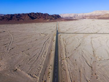 Çöl yolu, kuru çöl manzarasıyla çevrili iki şeritli bir yolun havadan görüntüsü.