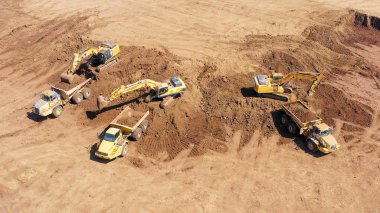Excavators, Articulated Hauler kamyonları ve daha fazlası gibi birden fazla ağır sanayi araçlarının çalıştığı geniş bir kazı alanının hava görüntüsü.