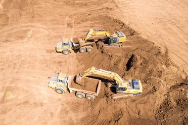 Excavators, Articulated Hauler kamyonları ve daha fazlası gibi birden fazla ağır sanayi araçlarının çalıştığı geniş bir kazı alanının hava görüntüsü.