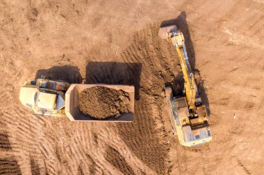 Kazıcıların eklemli nakliye kamyonlarına toprak yüklediği hava görüntüsü