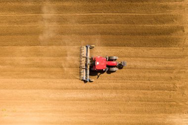 Kırmızı traktör yerleşim yerinin yakınında büyük bir tarla işliyor..