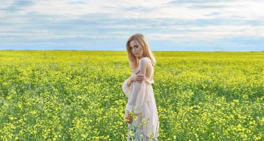 Sarı elbiseli kız sarı çiçekli bir tarlada oturuyor.