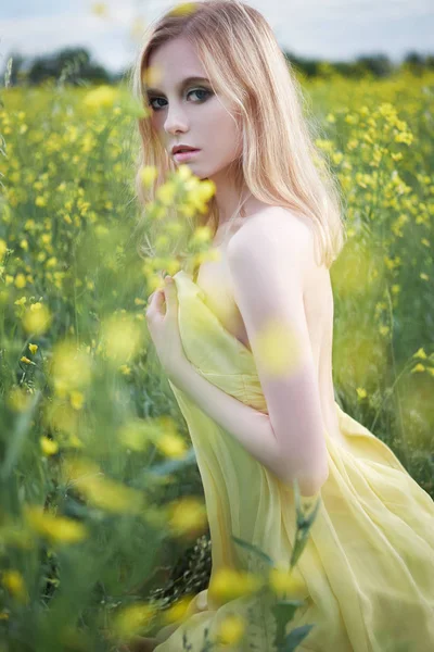Sarı elbiseli kız sarı çiçekli bir tarlada oturuyor. — Stok fotoğraf